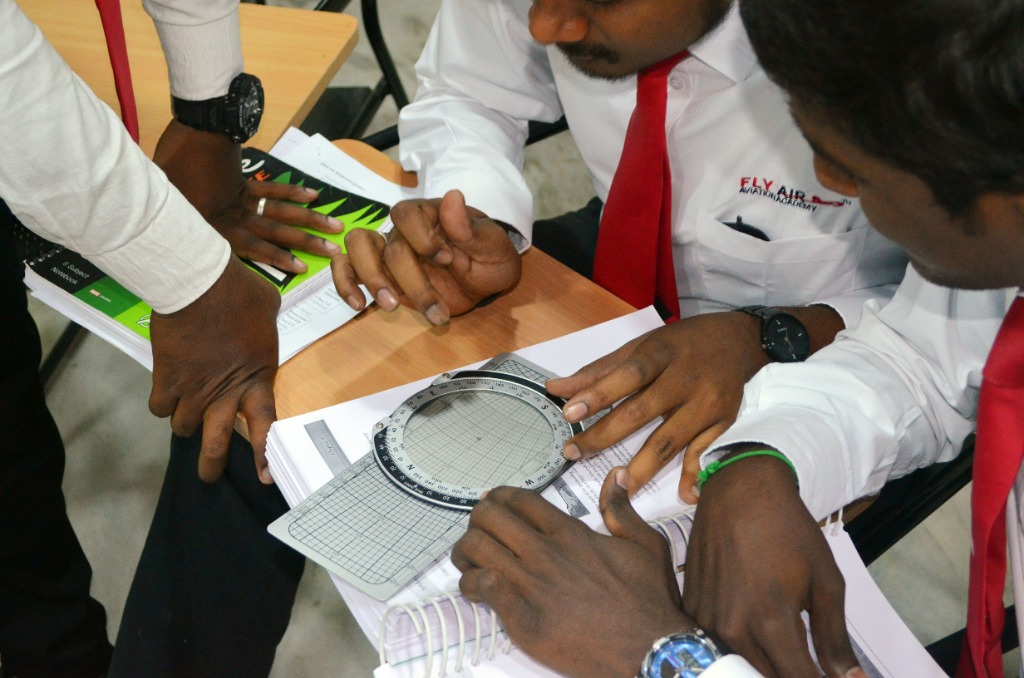 Pilot ground school students performing calculations using a flight computer and navigation chart
